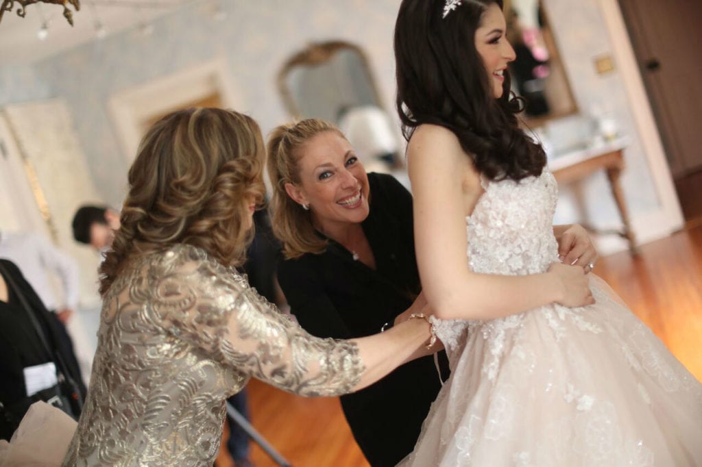 Bride getting wedding dress adjusted by attendants